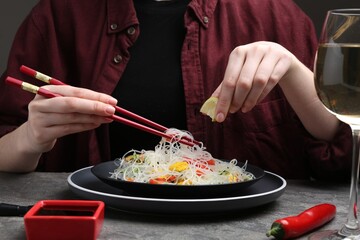 Stir-fry. Woman squeezing lime into tasty rice noodles with meat and vegetables at grey textured table, closeup