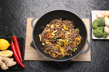 Stir-fry. Tasty noodles with vegetables, meat in wok and ingredients on dark textured table, flat lay