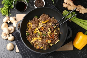 Stir-fry. Tasty noodles with meat and vegetables in wok served on dark textured table, flat lay