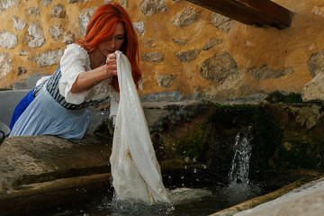 Mujer con vestido de epoca modernista lavando la ropa en lavadero antiguo de la población de Sella, España