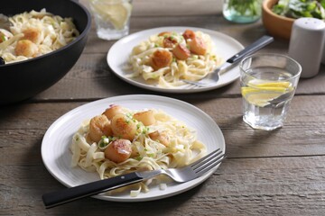 Delicious scallop pasta with onion served on wooden table, closeup