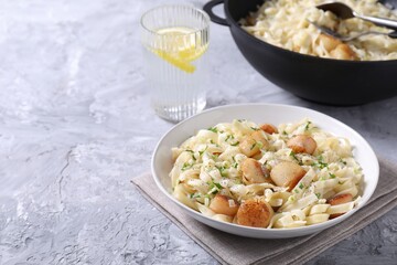 Delicious scallop pasta with spices in bowl and glass of water on gray textured table, closeup. Space for text