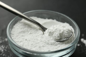 Baking powder in bowl and spoon on black table, closeup