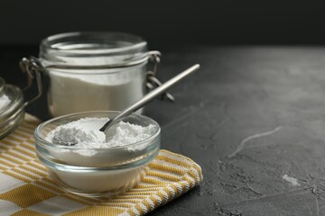 Fototapeta na wymiar Baking powder in bowl, jar and spoon on black textured table, closeup. Space for text