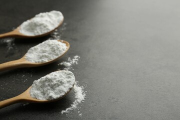 Baking powder in spoons on grey textured table, closeup. Space for text