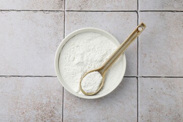 Baking powder in bowl and spoon on light tiled table, top view