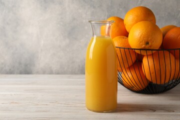 Tasty fresh oranges and juice in jug on white wooden table, space for text
