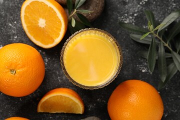 Tasty fresh oranges, juice, stones and leaves on black table, flat lay