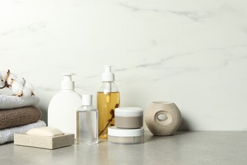 Bath accessories. Personal care products, terry towels and cotton flowers on gray table near white marble wall