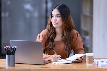 A young woman sitting at working desk in front of a laptop in the office.