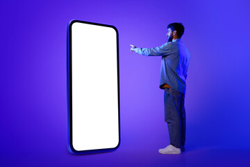 guy stands scrolling on huge smartphone, neon blue studio backdrop