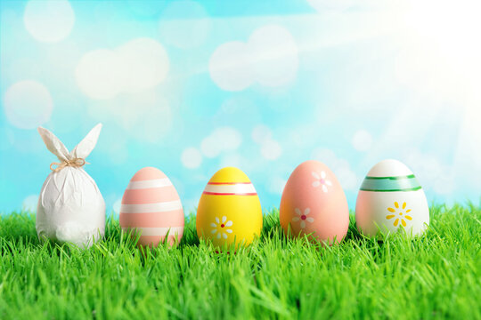 Easter egg wrapped in a paper in the shape of a bunny with colorful Easter eggs on green grass. Spring holidays concept.