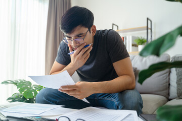 Thoughtful man holding paper work documents and pen touching chin with thoughtful expression.