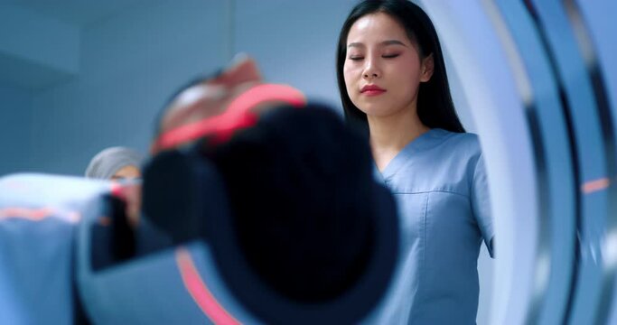 Friendly doctor finishing magnetic resonance tomography. Close up of patient lying at MRI capsule. MRI equipped cabinet. Undergoing tomography examination. Smiling doctor adjusting CT scanner.