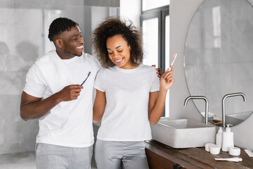 black couple brushing teeth in morning in modern bathroom indoors