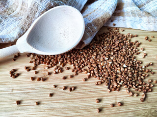 Buckwheat scattered on textured fabric and in a wooden spoon. Grits for cooking. Texture,...