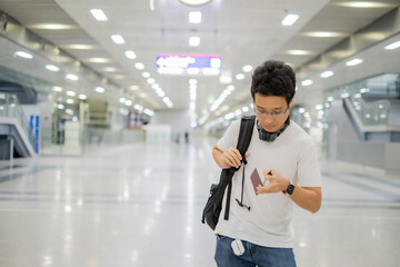 Young Asian Traveler with glasses in white t- shirt standing at airport, looking at passport,...