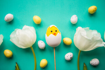Easter composition - tulips, toy chicken  and quail eggs on bright green background, top view