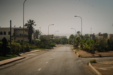 Agadir, Morocco - February 25, 2024 - A quiet street with lamp posts and lush greenery on both...
