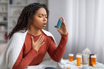 Young black woman experiencing an asthma attack, using an inhaler for relief