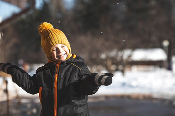 Portrait of a little boy in a yellow hat. The child runs through puddles on the farm, has fun and...