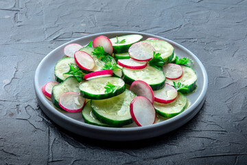 Fresh cucumber and radish salad with parsley. Simple vegan recipe on a black stone background - 752172475