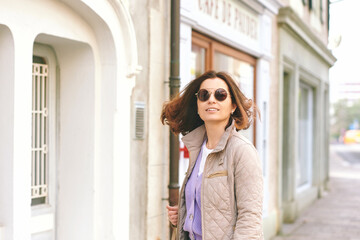 Outdoor portrait of happy middle age woman walking outside, wearing beige quilted jacket and sunglasses, nice sunny day - 752174409
