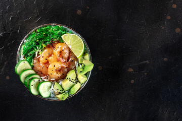 Shrimp poke bowl with avocado, cucumbers, wakame, and lime, shot from above on a black background...