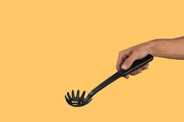 Black male hand holding plastic kitchen skimmer on yellow background.