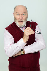 An elderly gray-haired man with a beard looks at the camera in surprise.