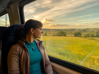 Cheerful woman admires the scenic green countryside while traveling by train