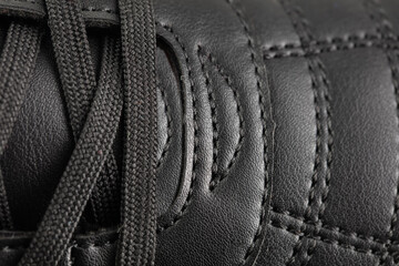 Part of a black leather sneaker with stitching close-up.