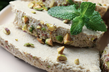 Pieces of tasty halva with pistachios and mint on table, closeup
