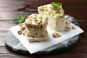 Pieces of tasty halva with pistachios and mint on wooden table, closeup