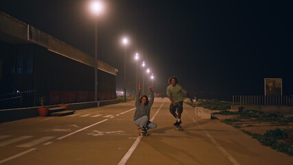 Carefree hipsters riding skateboard at twilight street. Skaters couple training