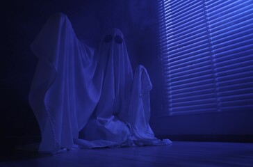 Creepy ghost. Woman covered with sheet near window in blue light, low angle view. Space for text