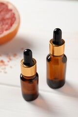 Grapefruit essential oil in bottles on white wooden table, closeup