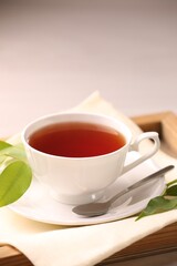 Aromatic tea in cup, saucer, spoon and green leaves on table
