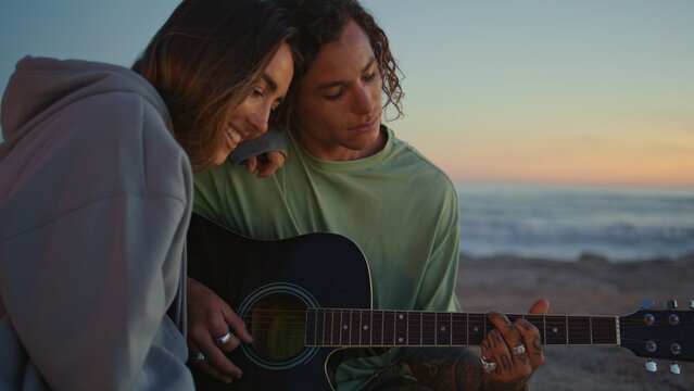 Tattooed man hands playing guitar at sunset closeup. Love couple dating at ocean