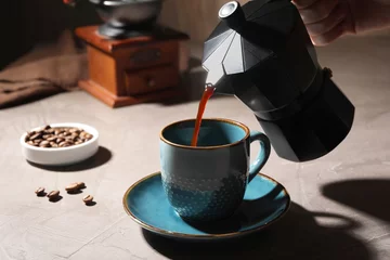  Pouring aromatic coffee from moka pot into cup at light table, closeup © New Africa