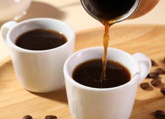 Pouring aromatic coffee from cezve into cup at wooden board, closeup