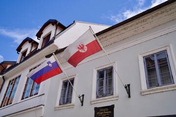 Old town of Slovenian City of Kranj with waving Slovenian flag and flag of City of Kranj on a summer day. Photo taken August 10th, 2023, Kranj, Slovenia.