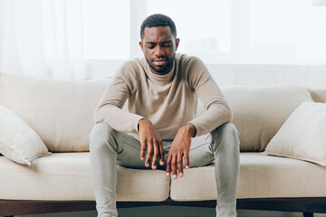 Stressed African American man suffering from a headache on a couch at home He looks tired, sick,...