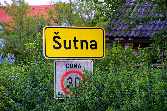 Close-up of yellow sign and speed limit 30 road sign at rural village of Sutna on a cloudy summer evening. Photo taken August 10th, 2023, Šutna, Kranj, Slovenia.