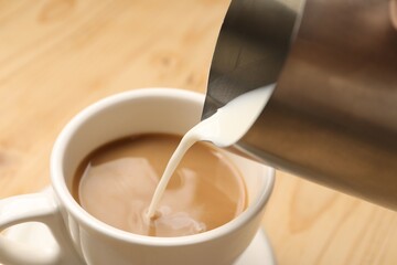 Pouring milk into cup at table, closeup