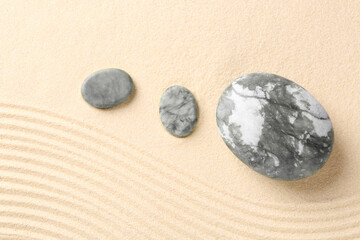 Zen garden stones on beige sand with pattern, flat lay