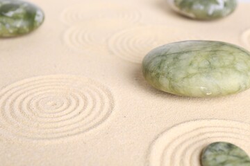 Fototapeta na wymiar Zen garden stones on beige sand with pattern, closeup