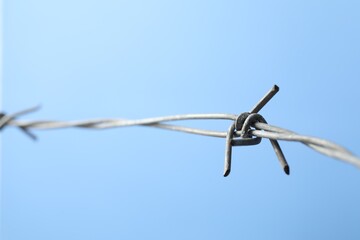 Metal barbed wire on light blue background, closeup