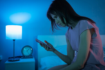 Young woman in bed using smartphone in night suffering from insomnia, uncomfortable sleeping...