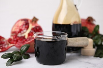 Tasty pomegranate sauce and branch on white marble table, closeup